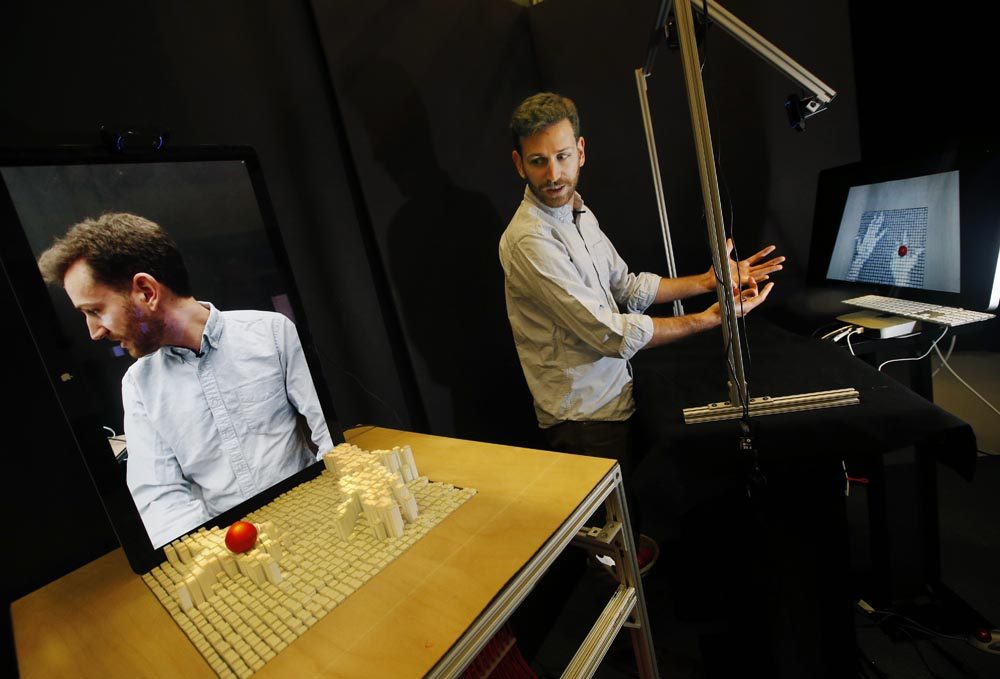 MIT graduate student  Sean Follmer, a researcher with MIT's Tangible Media Group, moves his hands in front of a depth-sensing camera, which sends signals to a motorized pin screen, far left, where a 3D image pops up to manipulate the red ball. (Elise Amendola/AP)