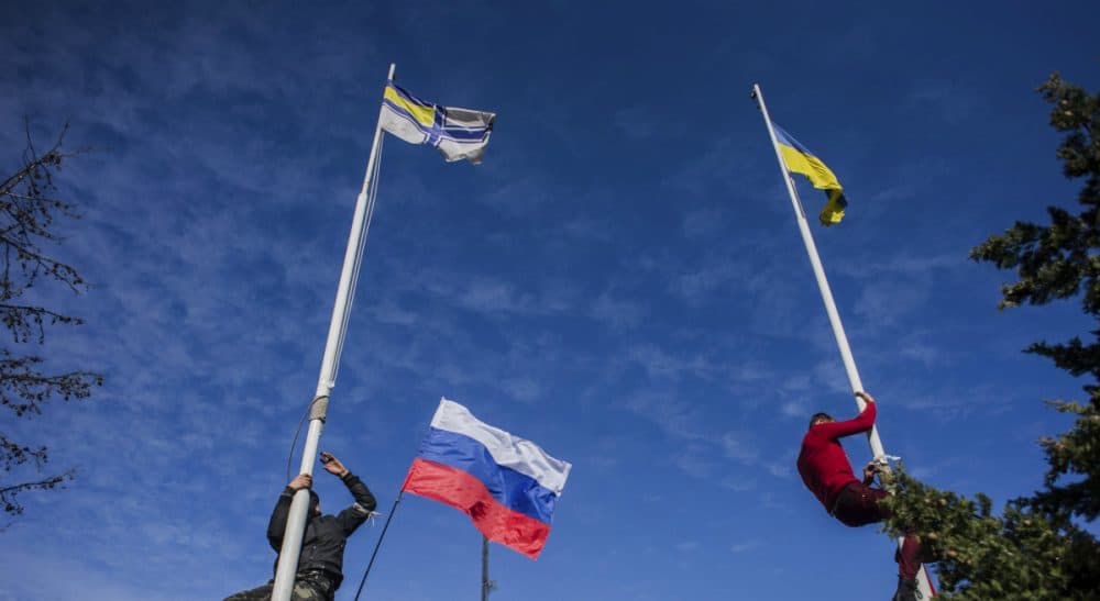 Members of the Crimean pro-Russian self-defense forces climb up to take down a Ukrainian flag, right, and a Ukrainian navy flag, left, at the Ukrainian navy headquarters in Sevastopol, Crimea, Wednesday, March 19, 2014. In center is a Russian flag. (Andrew Lubimov/AP)