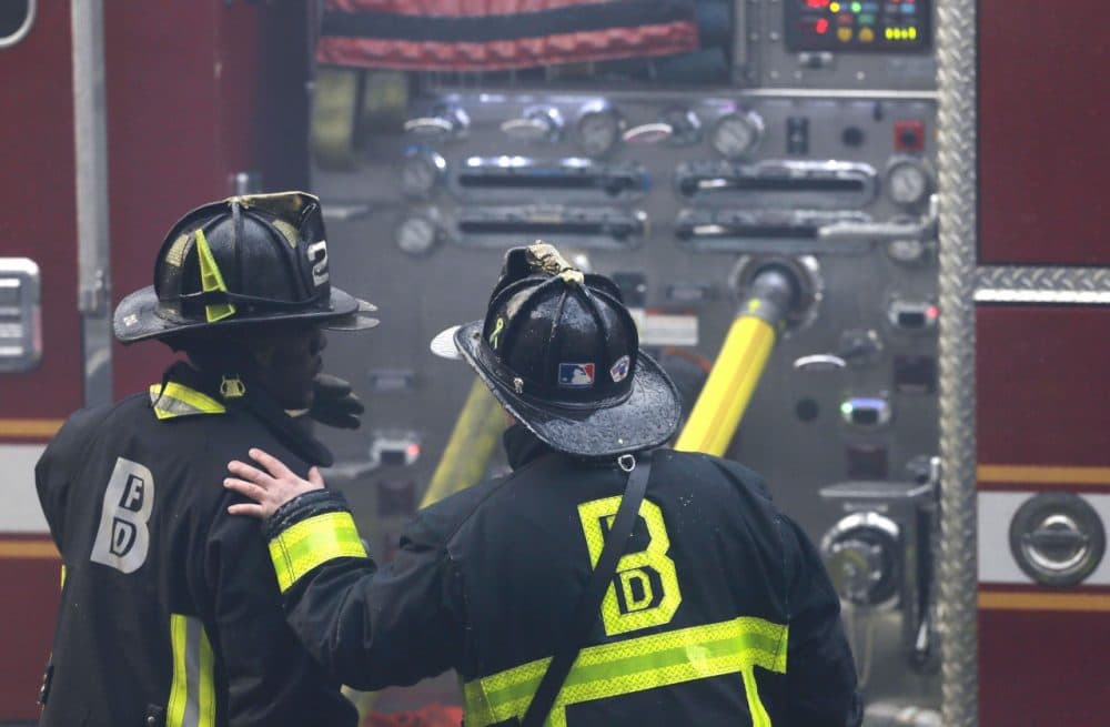 A firefighter places his hand on the shoulder of another at the scene of a multi-alarm fire at a four-story brownstone in the Back Bay neighborhood near the Charles River, Wednesday, March 26, 2014 in Boston. (AP)