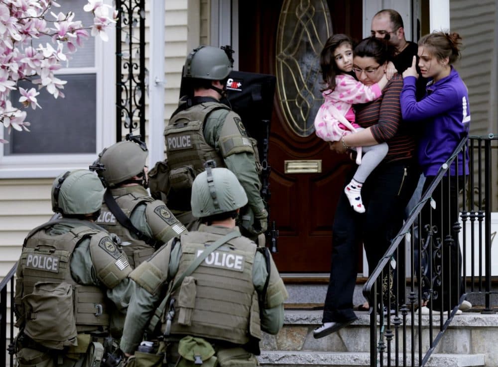 A woman carries a girl from their home as a SWAT team searching for a suspect in the Boston Marathon bombings enters the building in Watertown. (Charles Krupa/AP)