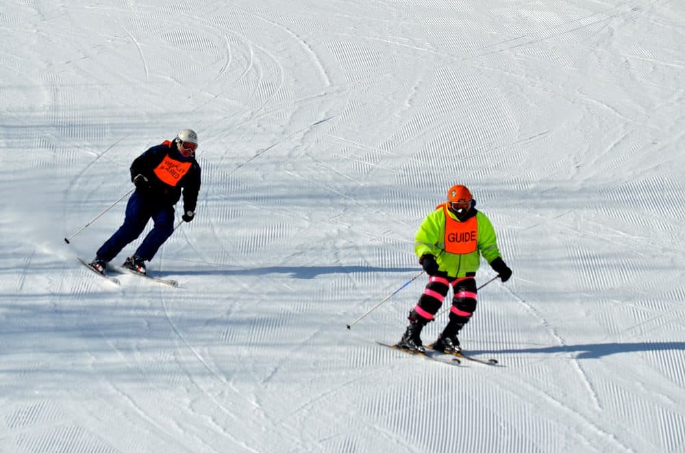 Tony Carleton, right, guided his friend, Dick Perkins, down the slopes at Wachusett Mountain Ski Area in Princeton, Mass., in 2016. Like other ski resorts in the state, Wachusett has relied on artificial snow this season. (Sharon Brody/WBUR)