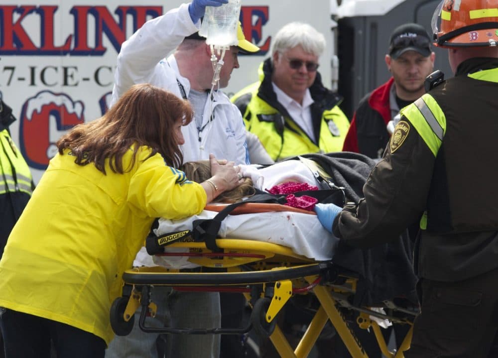 Alicia Shambo, in the yellow jacket, comforts Victoria McGrath, seriously injured in the bombing of the Boston Marathon,  as medics prepare to put McGrath into an ambulance Monday, April 15, 2013. (Jeremy Pavia/AP)