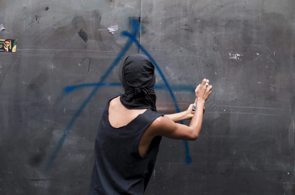 A young man spray paints an anarchist symbol on a kiosk during a march by anarchists on Labor Day in Mexico City, Thursday, May 1, 2014. Thousands of people, many calling for greater worker rights and protections, participated in various marches around the city center. (Rebecca Blackwell/AP)