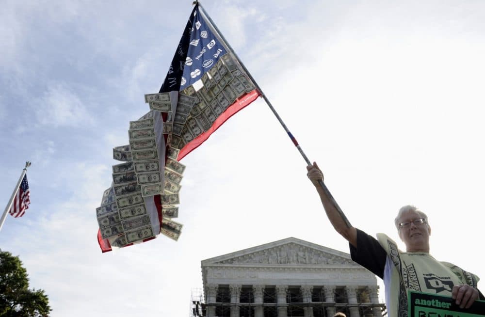 David Barrows of Washington holds a flag covered in money and corporate logos during a demonstration outside. (Susan Walsh/AP)