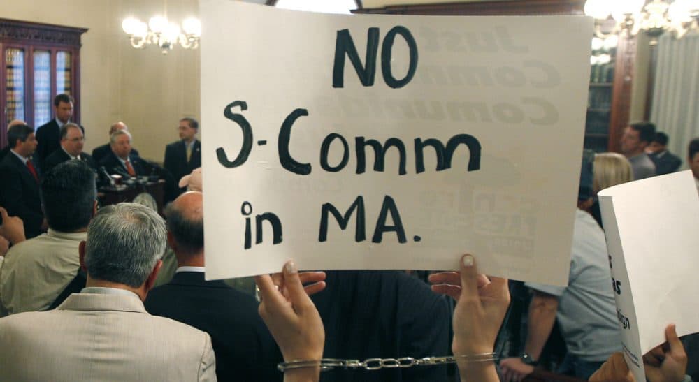 In this file photo, protesters wearing handcuffs holds up signs urging the stop of the &quot;Secure Communities&quot; program, or &quot;S Comm,&quot; at a news conference held by Massachusetts county sheriffs at the Statehouse in Boston, Wednesday, Sept. 28, 2011. (Charles Krupa/AP) 