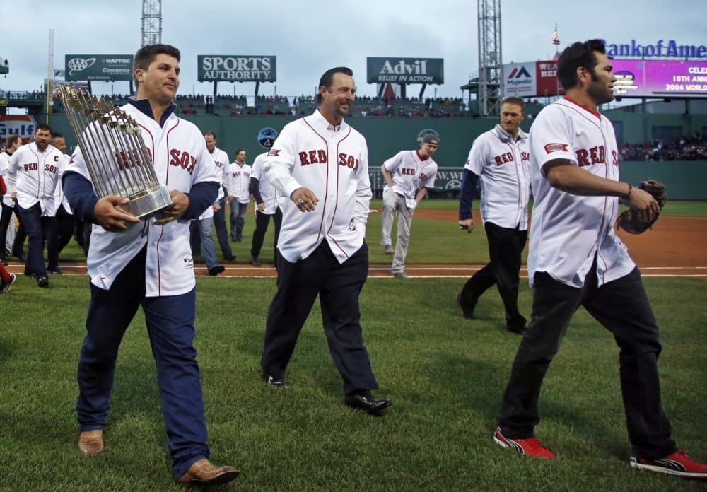 Former Boston Red Sox pitcher Keith Foulke, left, carries the 2004 World Series trophy walking off the field with 2004 teammates, Tim Wakefield, middle, and Johnny Damon, right, after they were honored at Fenway Park prior to a baseball game against the Atlanta Braves in Boston, Wednesday, May 28, 2014. (Elise Amendola/AP)