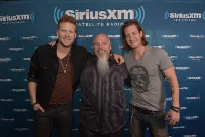 Brian Kelley and Tyler Hubbard of the band Florida Georgia Line embrace SiriusXM country music programmer John Marks, who helped propel their group to national prominence. (SiriusXM)