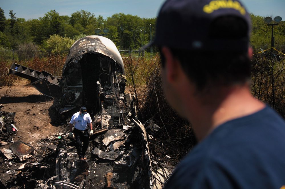Wreckage lay at the scene Monday in Bedford,  where a private plane plunged down an embankment and erupted in flames during a takeoff attempt at Hanscom Field Saturday night. Seven people died in the crash.  (Fred Thys/WBUR)
