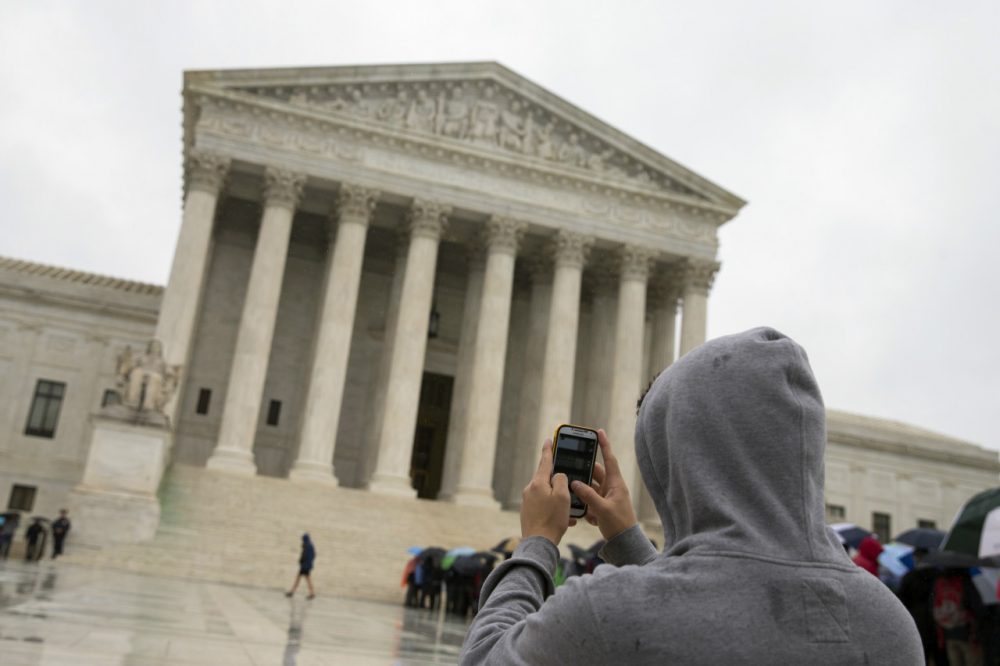 This April 29, 2014 file photo shows a Supreme Court visitor using his cellphone to take a photo of the court in Washington. A unanimous Supreme Court says police may not generally search the cellphones of people they arrest without first getting search warrants. The justices say cellphones are powerful devices unlike anything else police may find on someone they arrest. (AP)