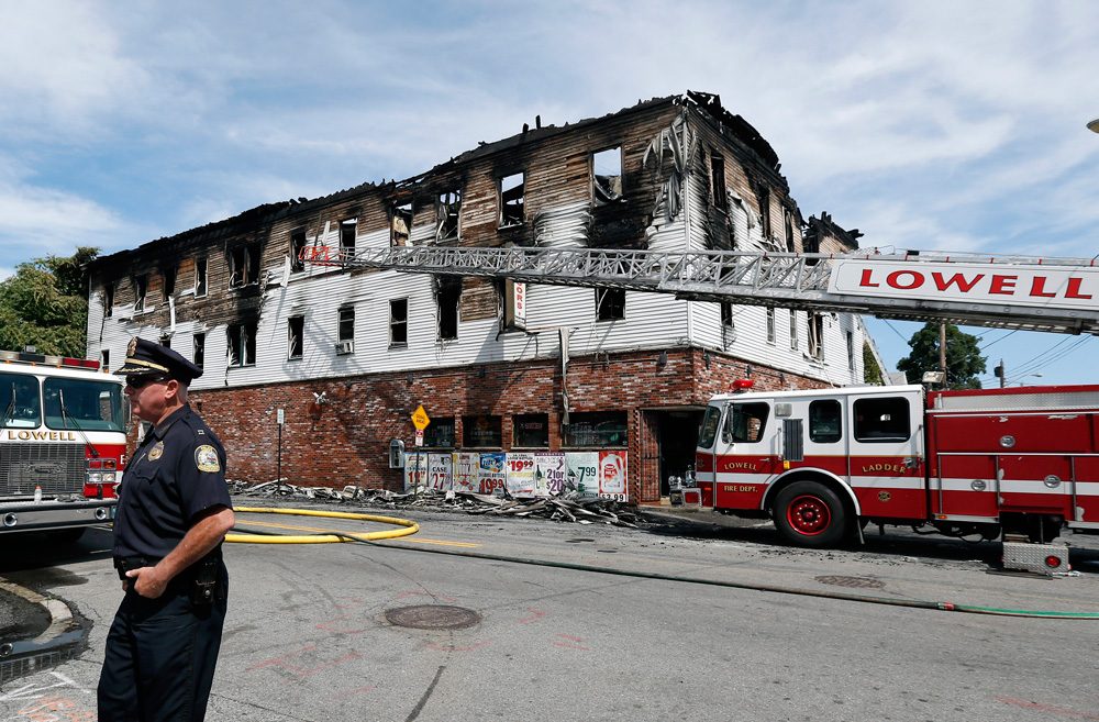 A policeman secures the scene last Thursday of a burned three-story apartment and business building in Lowell, where officials said seven people died in a fast-moving pre-dawn fire. (Elise Amendola/AP)