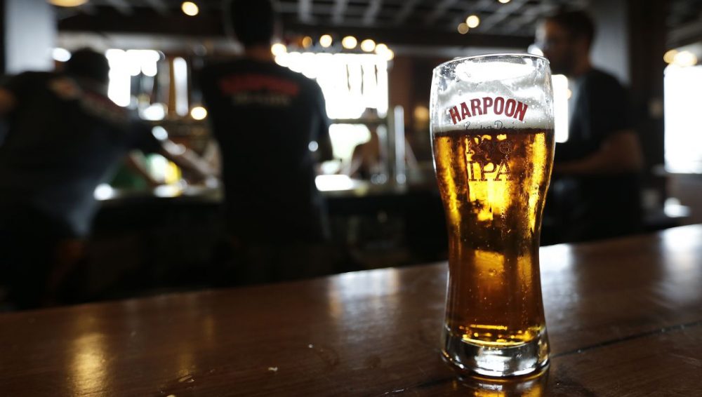 In this July 1, 2013 photo a glass of Rich and Dan's Rye IPA rests on the counter as bartenders pour drafts for patrons in the Beer Hall at the Harpoon Brewery in the Seaport District of Boston. (Charles Krupa/AP)