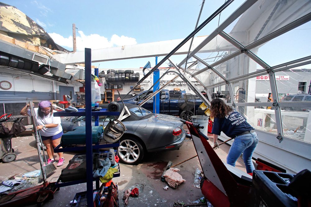 Master Auto manager Marie Annaloro, left, and Victoria Ohlson sweep glass and debris in the garage where the roof blew off during the tornado that touched down in Revere Monday. (Elise Amendola/AP)