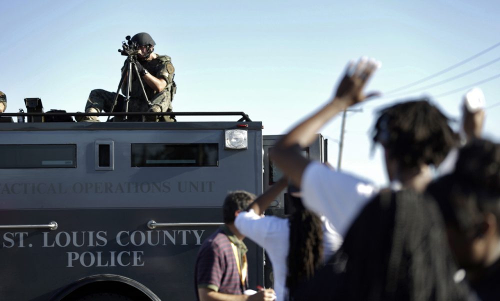 A member of the St. Louis County Police Department points his weapon in the direction of a group of protesters in Ferguson, Mo. on Wednesday, Aug. 13, 2014. On Saturday, Aug. 9, 2014, a white police officer fatally shot Michael Brown, an unarmed black teenager, in the St. Louis suburb. (Jeff Roberson/AP)