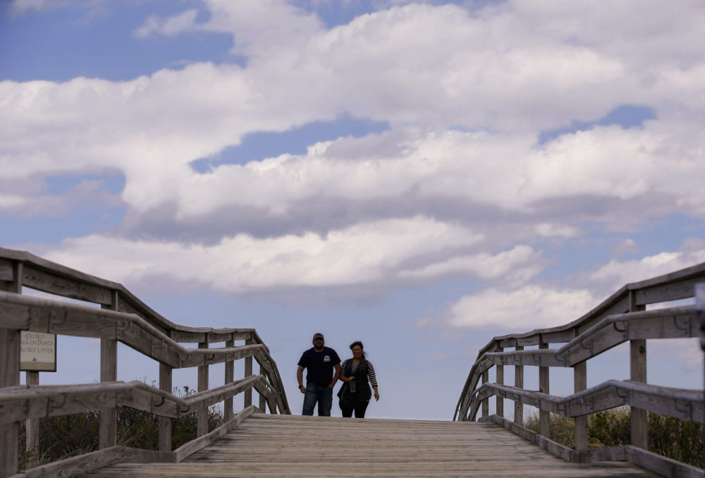 Two people walk across a beach bridge in the warmth of a spring afternoon on Duxbury Beach in May 2014 in Duxbury, Mass. (Stephan Savoia/AP)