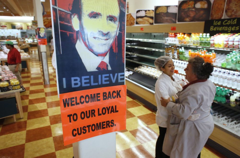 Market Basket employees Cristhian Romero, of Chelsea, Mass., second from right, and Tracie Parker, of Lynn, Mass., right, embrace near a likeness of Arthur T. Demoulas, top, at a Market Basket supermarket location, Thursday, Aug. 28, 2014, in Chelsea. A six-week standoff between thousands of employees of the New England supermarket chain and management has ended with the news that beloved former CEO Demoulas is back in control after buying the entire company. (AP)