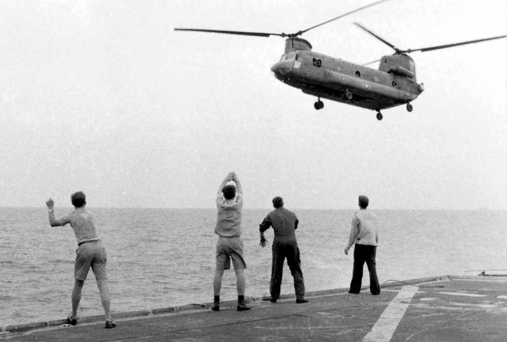 In this April 29, 1975 photo provided by courtesy of American Experience and Hugh Doyle, aboard the USS Kirk, crew members signal the Chinook to hover over the deck and drop its passengers out. (AP)