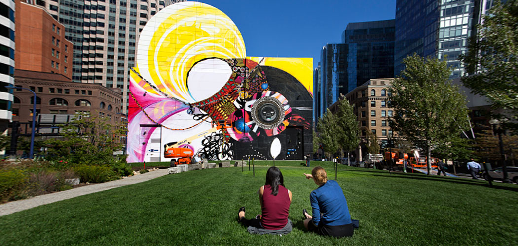 Two women point out elements of the new Dewey Square mural during a lunch break in the park. (Jesse Costa/WBUR)