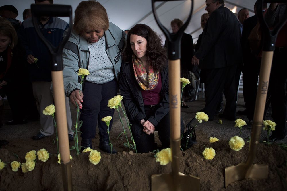 Myrnairis Cepeda, left, sets a yellow carnation into the ground in honor of her daughter who was killed in a car accident in the U.S. after several tours of duty overseas. Maggie Brothers,  right, is an Army Survivor Outreach Services Support Coordinator for Massachusetts whose husband died from exposure to radiation in Qatar. (Jesse Costa/WBUR)
