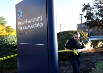 A Braintree cop places police tape around a Harvard Vanguard Medical Associates sign on Sunday. A patient there complained of Ebola-like symptoms, briefly closing the center. (Steven Senne/AP)