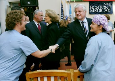At rear left is Boston Mayor Thomas Menino, pictured standing near, Sen. Edward M. Kennedy, D-Mass., shakes hands with nurse Janet Killarney while visiting the Boston Medical Center in 2004. (Charles Krupa/AP)