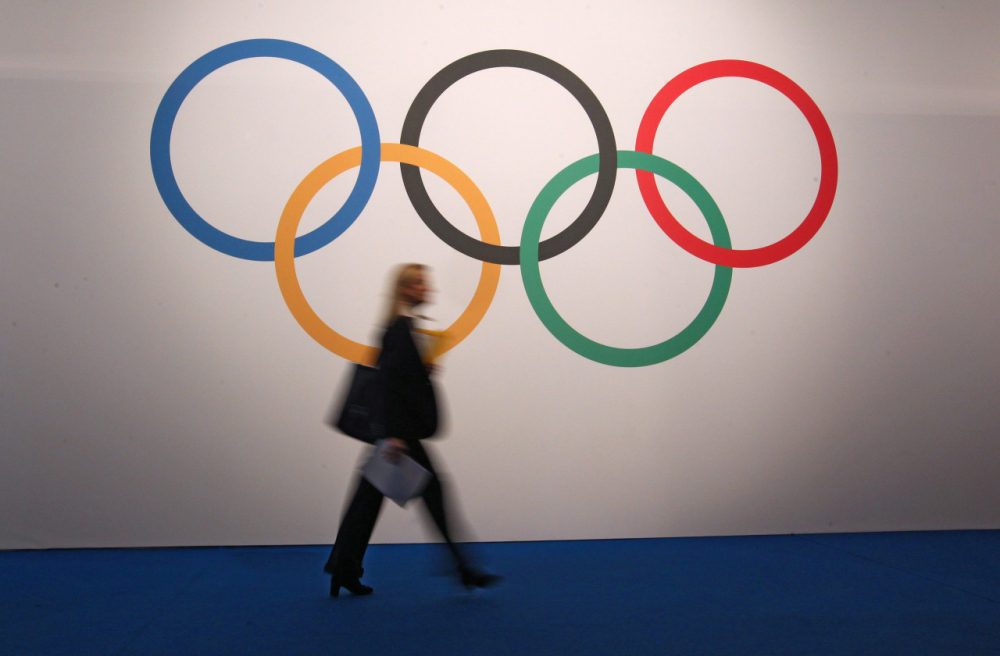 A woman walks in front of a board showing Olympics rings at the 127th International Olympic Committee session in Monaco, Monday, Dec. 8, 2014. (AP)