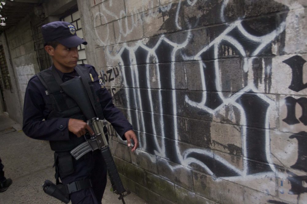In this March 7, 2014 file photo, a member of the Salvadoran National Police walks next to graffiti of the Mara Salvatrucha gang painted on a wall during an anti-gang operation in San Salvador. Gang violence is prevalent in the Central American nation, and murders are up this year. 