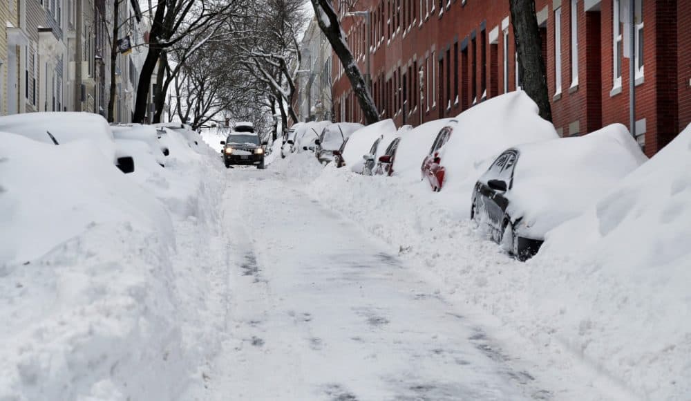 A car makes its way down a street filled with snowed-in vehicles in Boston's Charlestown section Wednesday. Gov. Baker announced a statewide travel ban as Monday's snowstorm got underway. (Elise Amendola/AP)