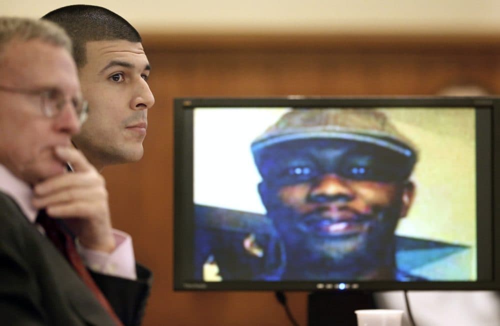 Aaron Hernandez listens during the first day of testimony in his murder trial Thursday. An image of Odin Lloyd, who Hernandez is charged with killing, is displayed on the monitor at right. (Steven Senne/AP)