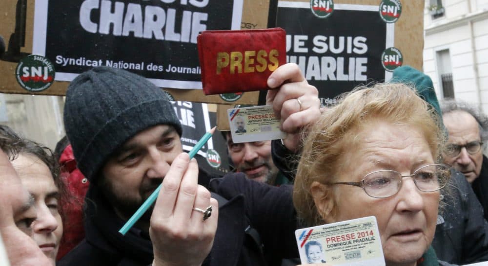 Journalists show their press cards and a pencil during a minute of silence outside the Charlie Hebdo newspaper in Paris, Thursday, Jan. 8, 2015, a day after masked gunmen stormed the offices of a satirical newspaper and killed 12 people. (François Mori/AP)