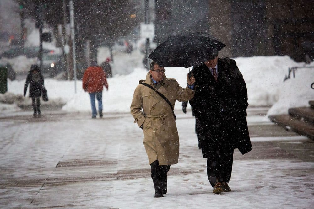 Two businessmen share an umbrella while walking down Dartmouth Street in Copley Square during a snowstorm on Feb. 5. (Jesse Costa/WBUR)