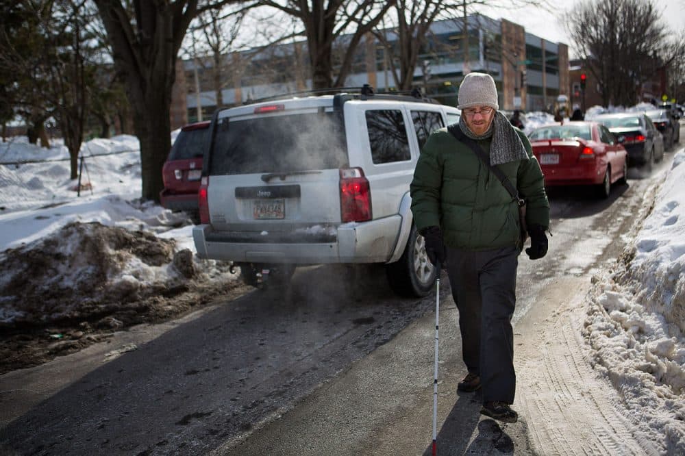 Kyle Robidoux, who's legally blind, walks on Shawmut Avenue Tuesday because the crosswalk curb cuts are not properly cleared and are blocked by snowbanks. (Jesse Costa/WBUR)