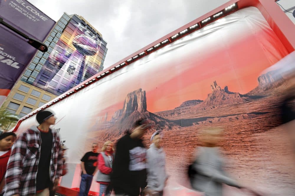 Pedestrians walk past a mural of an Arizona landscape as a banner of the Vince Lombardi Super Bowl Trophy decorates a building in Phoenix. The New England Patriots face the Seattle Seahawks in Super Bowl XLIX today, in Glendale, Ariz. (David Goldman/AP)