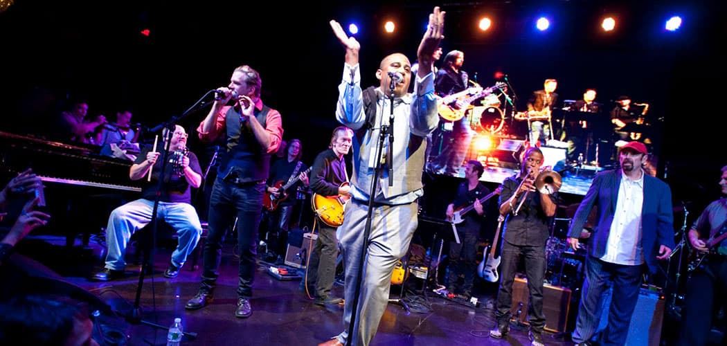 Glen David Andrews claps at the mic during the 2013 &quot;SuperGroup&quot; concert. Woody Giessmann sits at the piano at the left. (Michael Sparks Keegan)