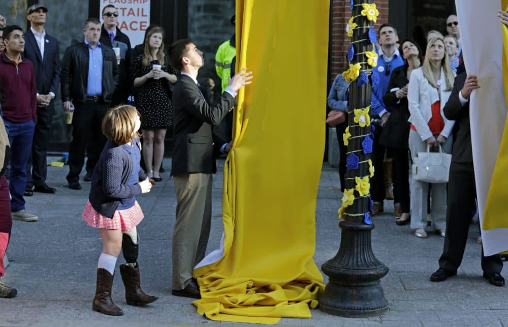 Boston Marathon survivor Jane Richard, left, watches as her brother Henry removes a drape covering a memorial honoring victims and survivors at one of two blast sites near the finish line in Boston. (Charles Krupa/AP)