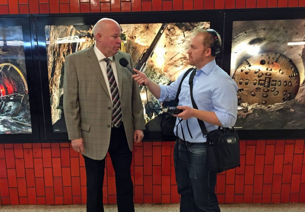 Here &amp; Now's Jeremy Hobson interviews MTA Chairman Thomas Prendergast in front of an exhibit of photos of MTA heavy construction projects. (Adam Lisberg/MTA)