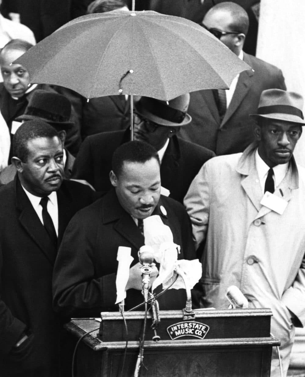 Dr. Martin Luther King Jr., protected by umbrella from rain, speaks to crowd on historic Boston Common, April 23, 1965. King led a civil rights march from the Roxbury section to the Common. He came to Boston, to lead the demonstration to protest segregation in schools, jobs and housing. (AP)