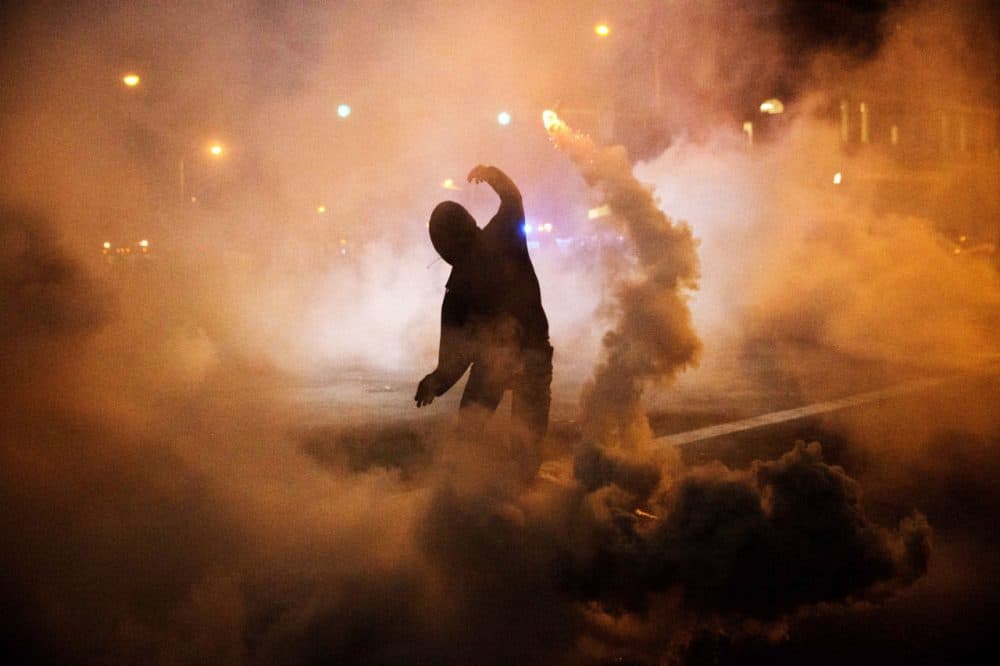 A protester throws a tear gas canister back toward riot police after a 10 p.m. curfew went into effect in the wake of Monday's riots following the funeral for Freddie Gray, Tuesday, April 28, 2015, in Baltimore. (David Goldman/AP)