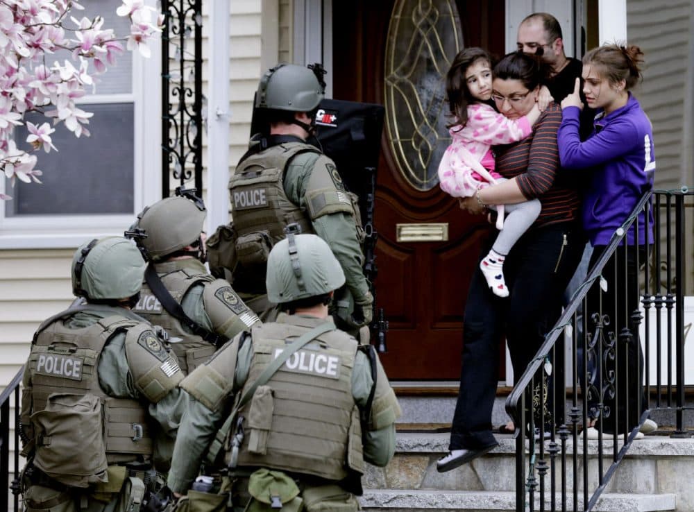 In this April 19, 2013, file photo, a woman carries a girl from their home as a SWAT team searching for a suspect in the Boston Marathon bombings enters the building in Watertown, Mass.  (AP)
