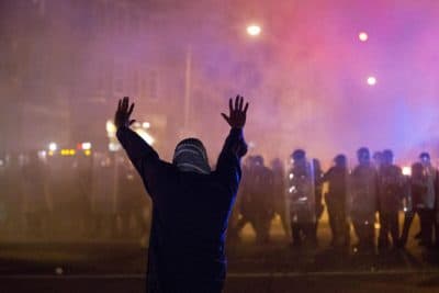 A protestor faces police enforcing a curfew Tuesday, April 28, 2015, in Baltimore. A line of police behind riot shields hurled smoke grenades and fired pepper balls at dozens of protesters to enforce a citywide curfew. (AP)