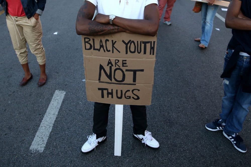 A young man holds a sign that reads 'Black youth are not thugs' as people participate in a dance party on North Ave., a day after Baltimore authorities released a report on the death of Freddie Gray, May 2, 2015 in Baltimore, Maryland. (Patrick Smith/Getty Images)