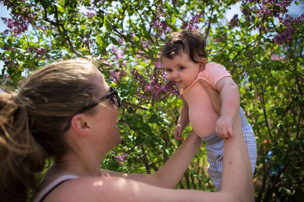At the Arnold Arboretum in Jamaica Plain on Friday, Hilary Samarel, of Cambridge, lifts her 3-month-old daughter, Noa, for her very first whiff of lilac flowers. (Jesse Costa/WBUR)