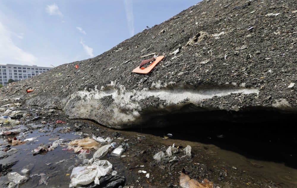 A 75-foot-high snow mound in the Seaport District has been reduced to a three-story pile of dirt and trash, including bicycles, traffic cones and even half a $5 bill, that remains encrusted in solid ice. Crews have been working for six weeks to clean away the trash as it breaks free from the mound. (Elise Amendola/AP)
