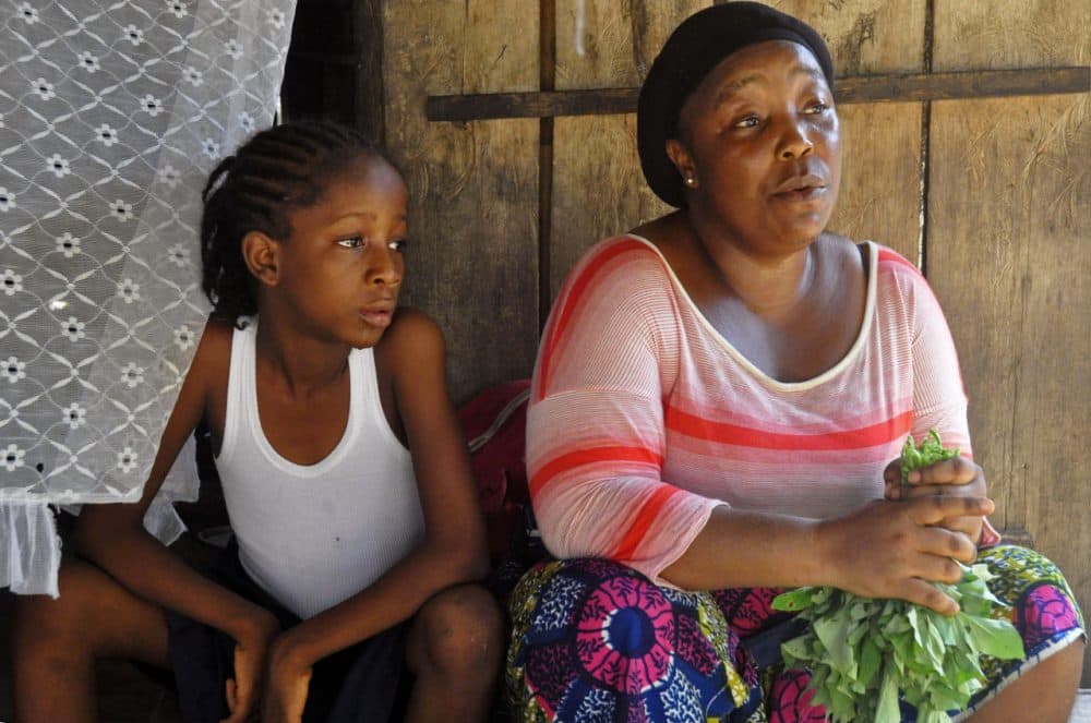 Mercy Kennedy (left), who lost her mother to Ebola, sits with her caregiver Martu Weefor (right) after school at her home in Monrovia, Liberia. Today, Mercy is thriving in the care of a family friend not far from where she used to live. (Abbas Dulleh/AP)