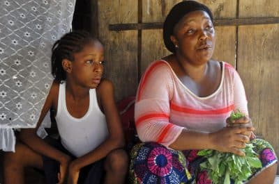 Mercy Kennedy (left), who lost her mother to Ebola, sits with her caregiver Martu Weefor (right) after school at her home in Monrovia, Liberia. Today, Mercy is thriving in the care of a family friend not far from where she used to live. (Abbas Dulleh/AP)