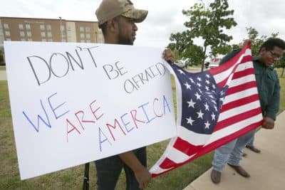 Joseph Offutt, left, and Raheem Peters hold a sign and a U.S. flag across the street from the Curtis Culwell Center, Tuesday, May 5, 2015, in Garland, Texas. A man, whose social media presence was being scrutinized by federal authorities, was one of two suspects killed in the Sunday shooting at this location that hosted a cartoon contest featuring images of the Muslim Prophet Muhammad. (AP)