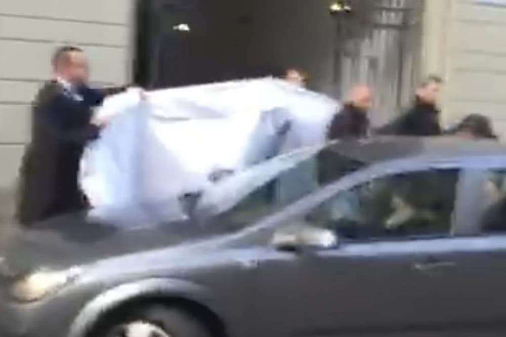In this picture taken from a cell phone video, hotel employees hold a blanket to hide the identity of a person led out of a side entrance of the Baur au Lac hotel to a waiting car in Zurich, Switzerland, Wednesday, May 27, 2015. (AP)