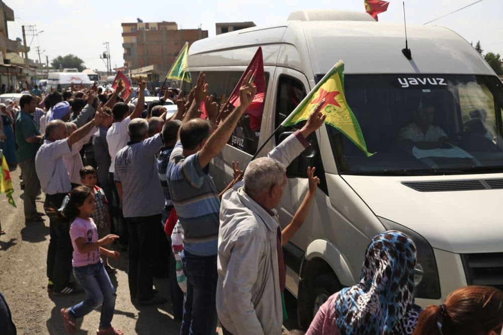 Kurdish people waving flags flash the V-sign and applaud while lining the road, as the convoy carrying the body of U.S. citizen Keith Broomfield, killed in fighting with the militants of the Islamic State group in Kobani, Syria, is driven by through Suruc, on the Turkey-Syria border, Thursday, June 11, 2015. (Lefteris Pitarakis/AP)