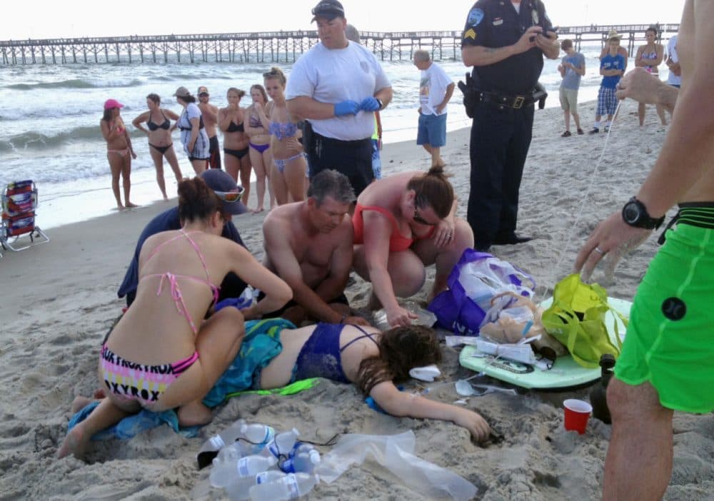Emergency responders assist a teenage girl at the scene of a shark attack in Oak Island, N.C., Sunday, June 14, 2015. Mayor Betty Wallace of Oak Island, a seaside town bordered to the south by the Atlantic Ocean, said that hours after the girl suffered severe injuries in a shark attack Sunday a teenage boy was also severely injured. (Steve Bouser/The Pilot, Southern Pines, N.C. via AP)