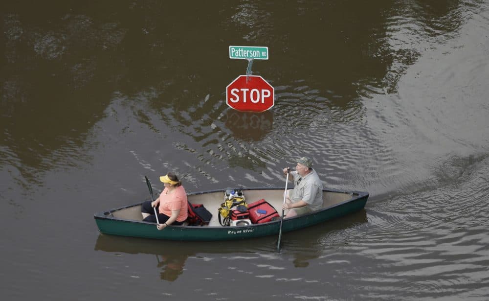 In this aerial photo, people canoe through floodwaters past a stop sign near Bear Creek Park Saturday, May 30, 2015, in Houston. The Colorado River in Wharton and the Brazos and San Jacinto rivers near Houston are the main focus of concern as floodwaters move from North and Central Texas downstream toward the Gulf of Mexico. (David J. Phillip/AP)