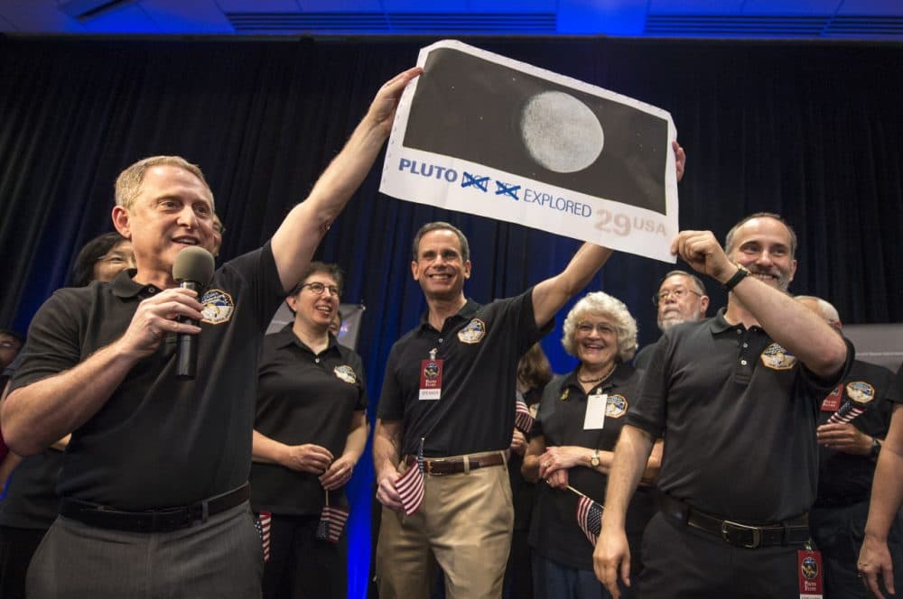 In this photo provided by NASA, New Horizons Principal Investigator Alan Stern of Southwest Research Institute (SwRI), Boulder, Colo., left, Johns Hopkins University Applied Physics Laboratory (APL) Director Ralph Semmel, center, and New Horizons Co-Investigator Will Grundy of the Lowell Observatory hold a print of a U.S. stamp with their suggested update since the New Horizons spacecraft made its closest approach to Pluto, at the Johns Hopkins University Applied Physics Laboratory (APL) in Laurel, Maryland. (Bill Ingalls/NASA via AP)
